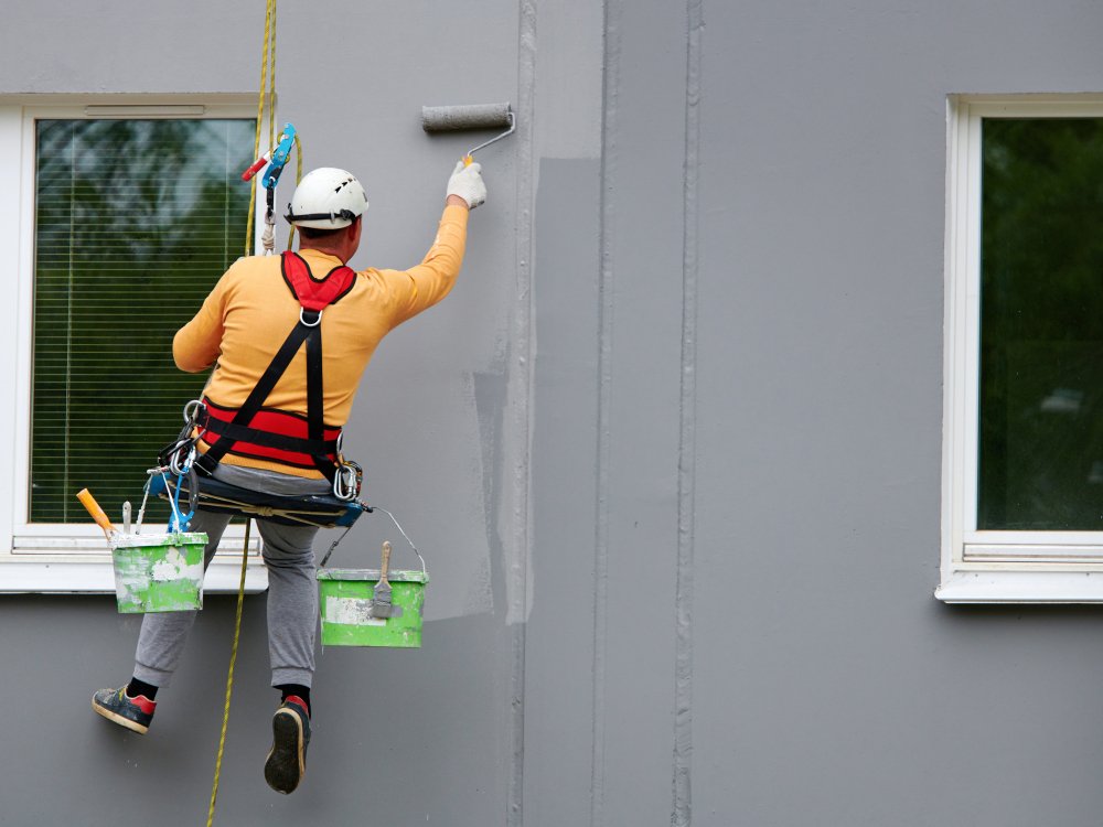 Worker,Hanging,On,Rope,And,Paints,Building,Wall,With,Roller.